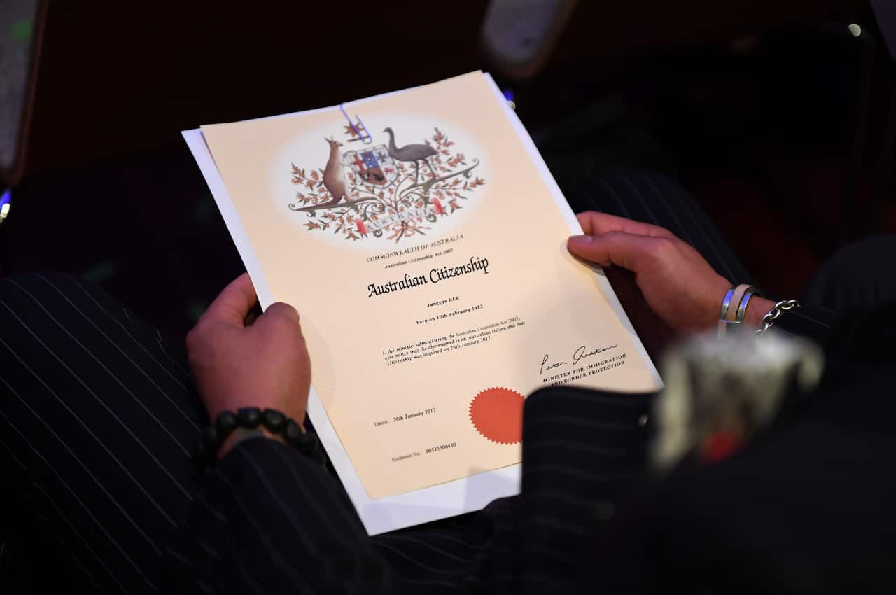 A close up of a woman holding an Australian Citizenship certificate in her lap. The document includes Australian native plants and emblems of a kangaroo and emu.