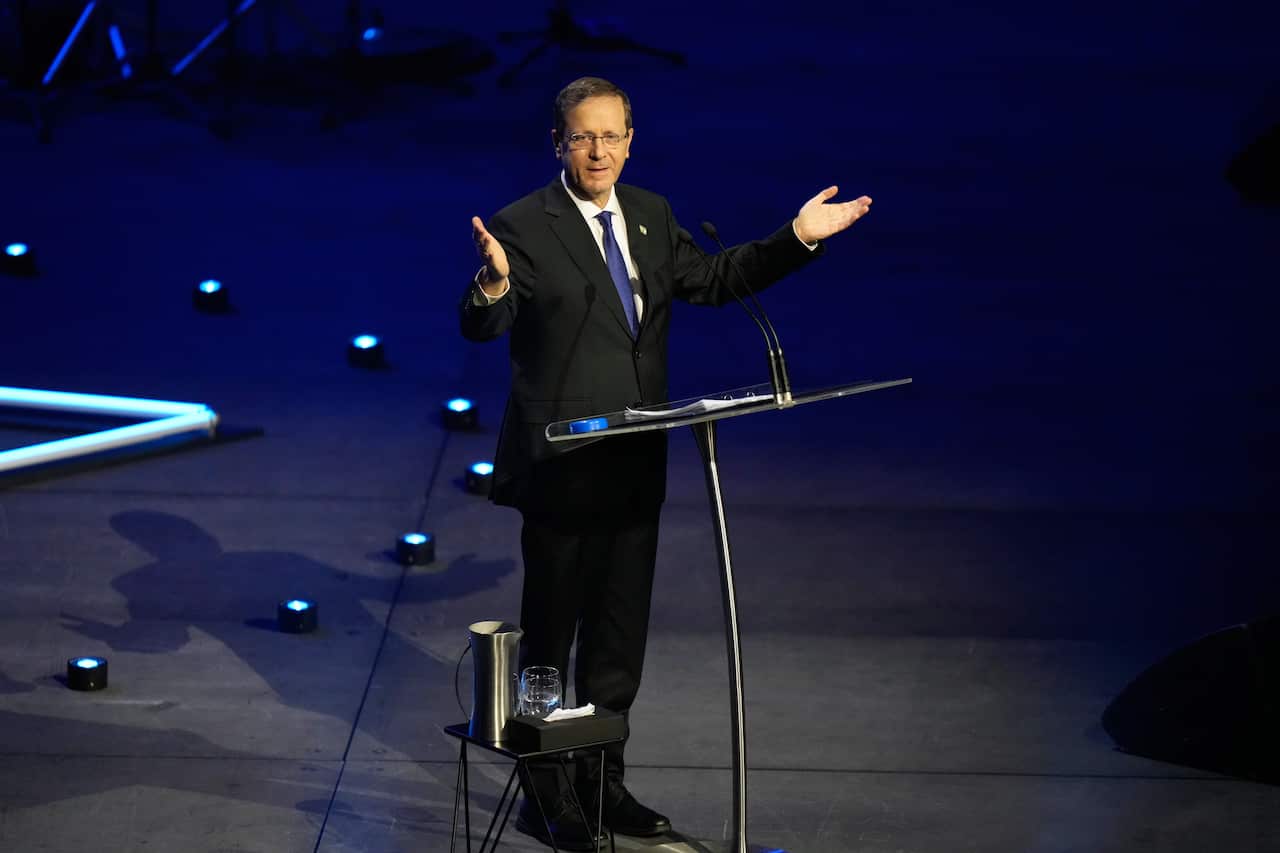 A white man in a black suit speaking on a stage before a lectern