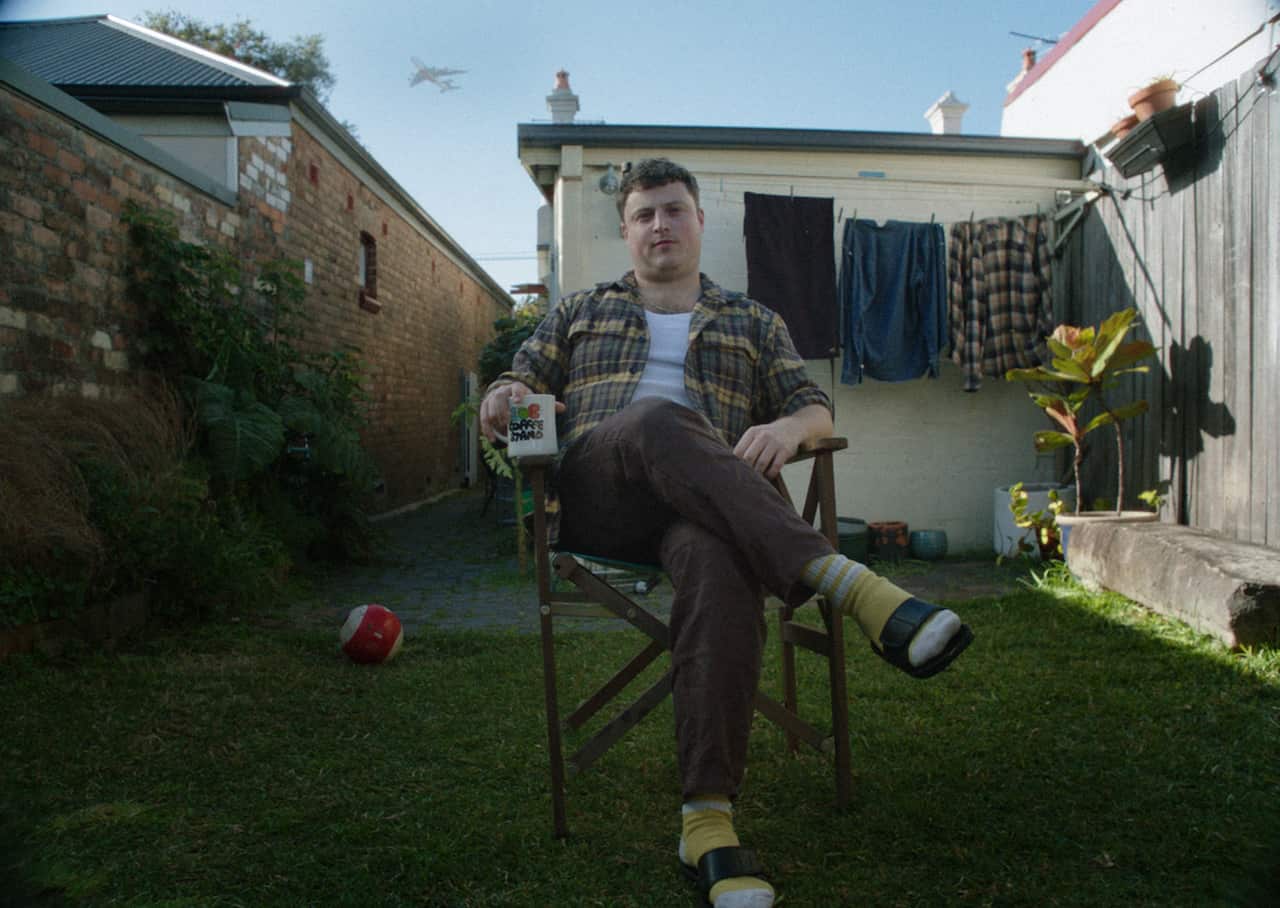 A man sitting cross-legged on a chair in his backyard.