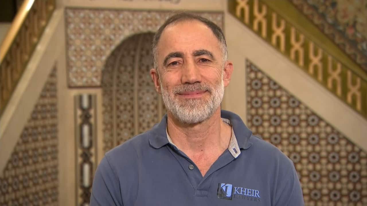 Um homem com uma camisa pólo azul está dentro de uma mesquita.