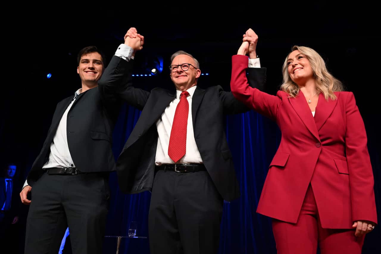 Anthony Albanese, hands raised with a young man and woman in a red blazer beside him.