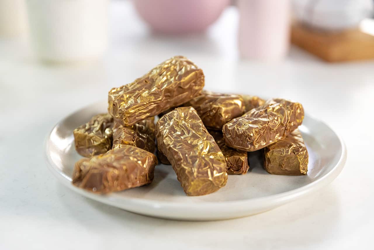 A pile of chocolate-coated bars sit on a round white plate. The bars glean with hints of gold. 