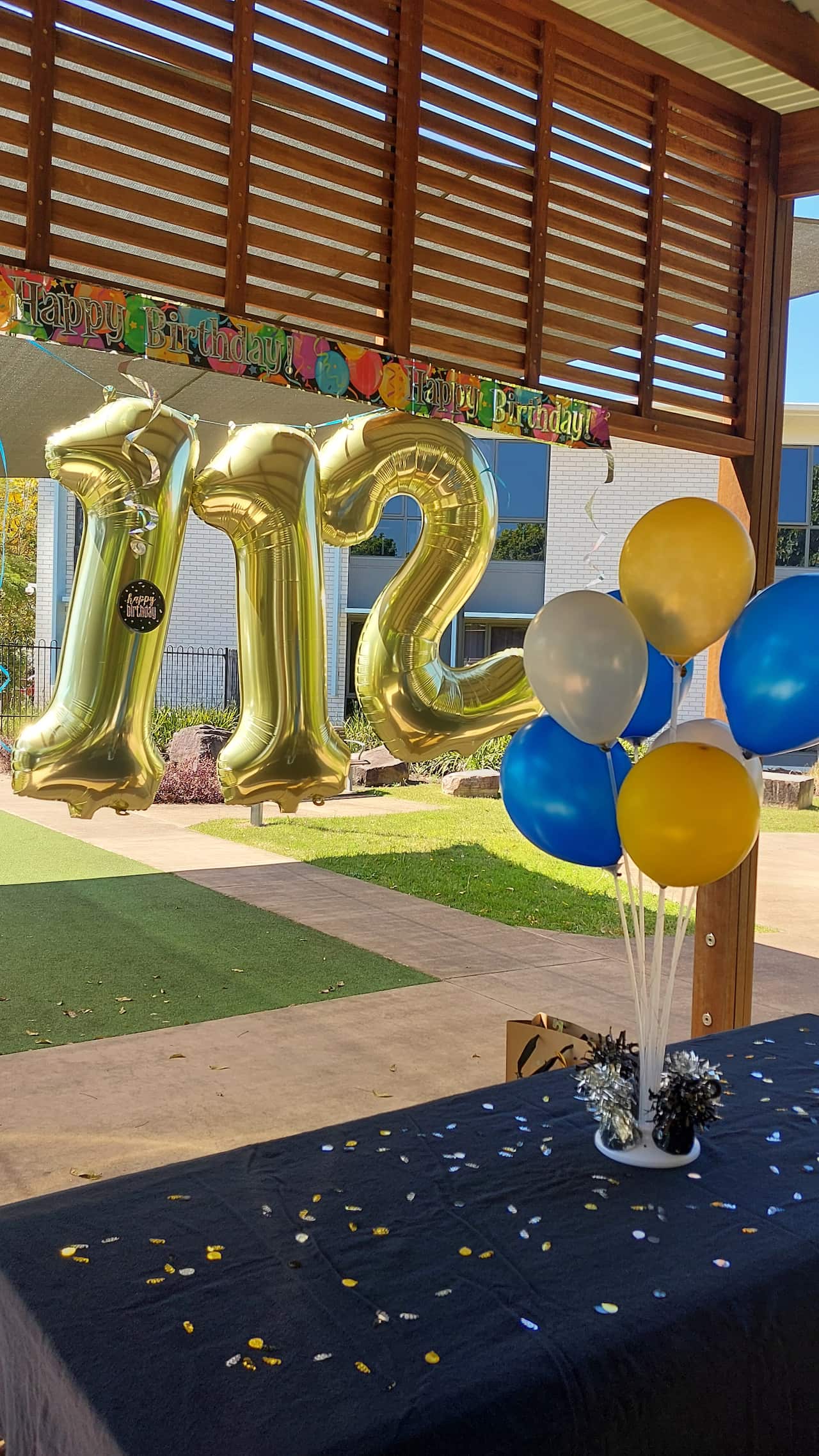 Gold balloons showing the numbers "112" and other blue and yellow balloons and confetti.