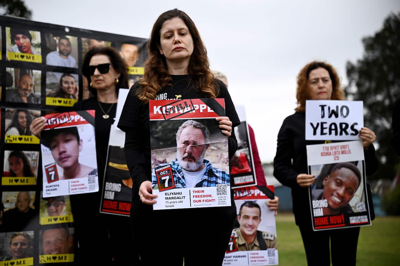 A group of women stands outdoors holding signs featuring photographs of people who are still held hostage in Gaza. 