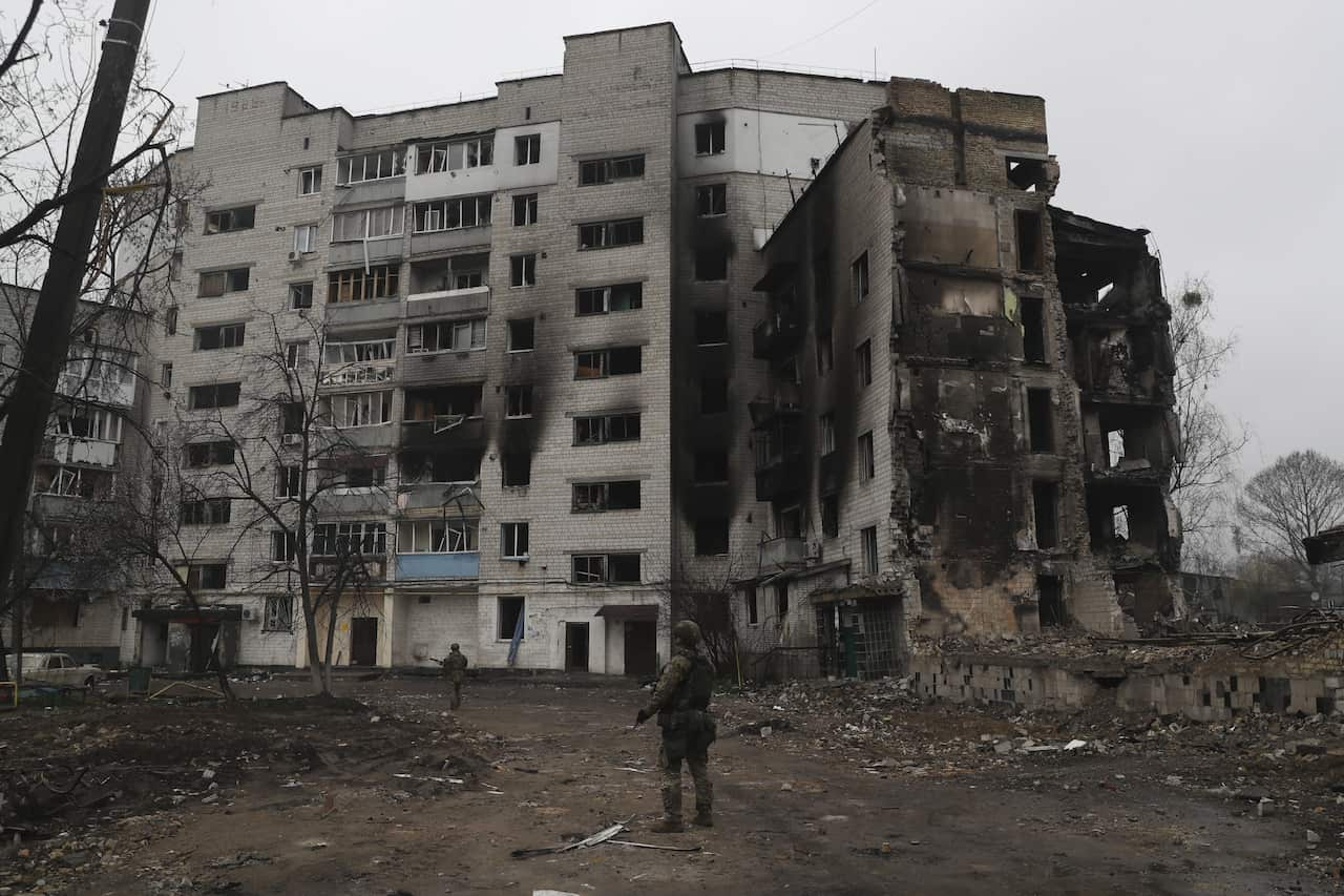 A soldier stands in front of a damaged residential building.