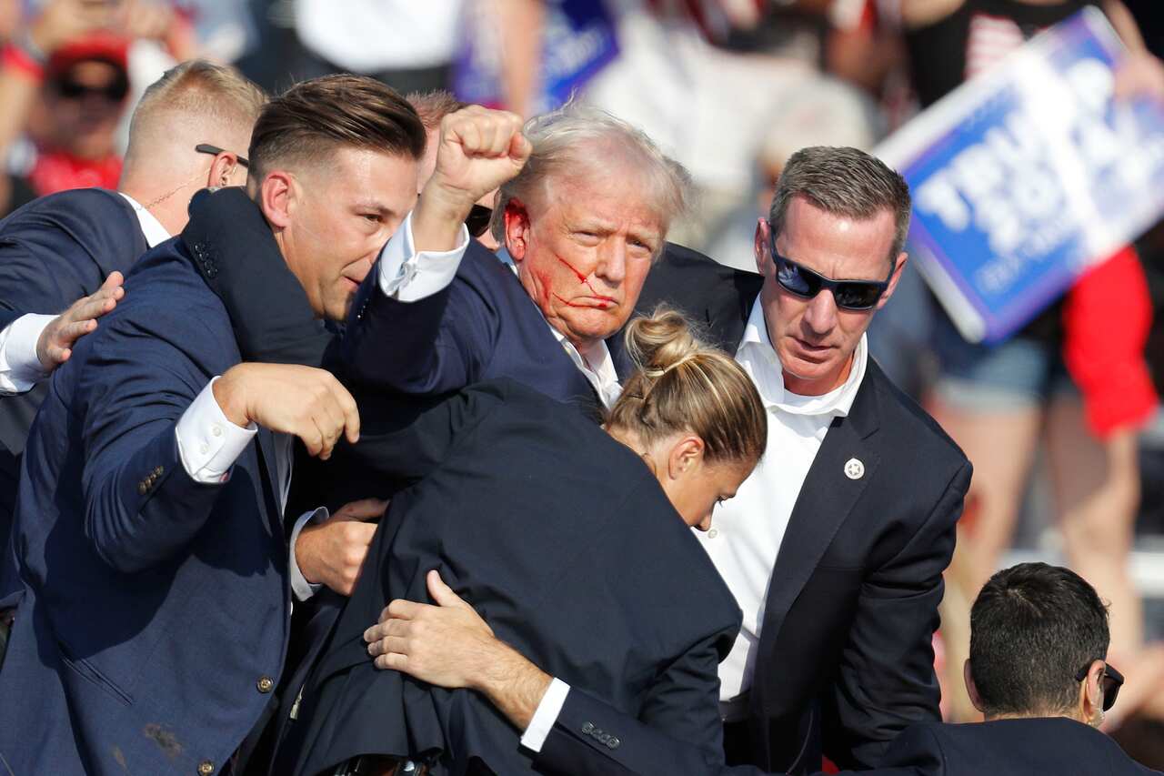 Former US President Donald Trump with blood on his face and surrounded by security staff. 