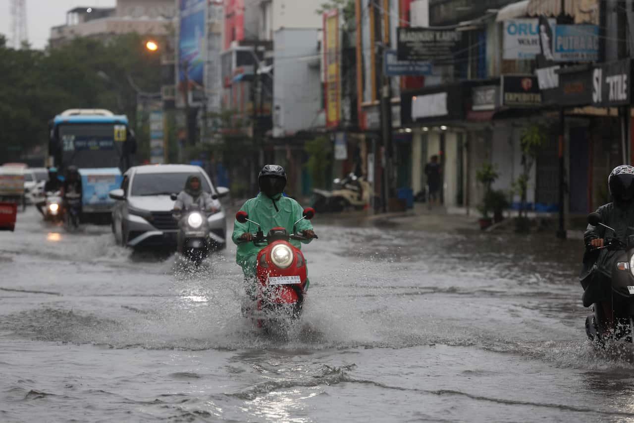 Motor cyclists drive through floodwaters