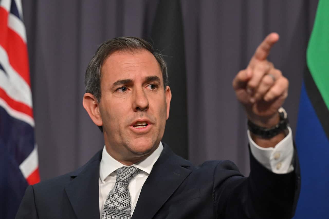 A man in a dark suit with a grey tie with the Australian and Aboriginal flags visible in the background