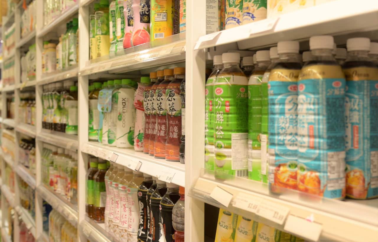 Supermarket shelves display drink bottles with Asian language labels.
