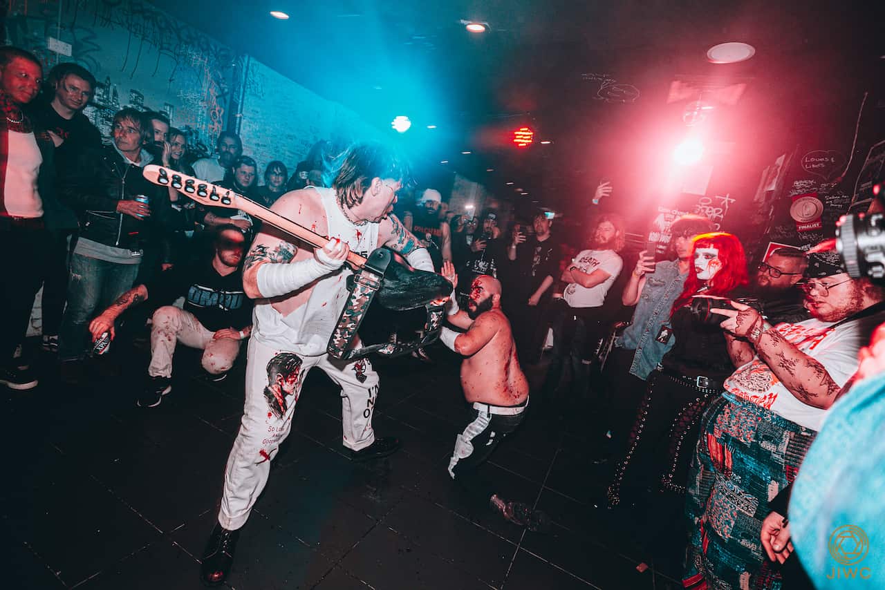 One man about to hit another with a guitar as a crowd watches on.