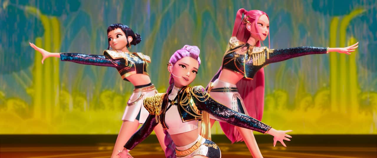 Three animated young women in colourful outfits strike a pose on stage.