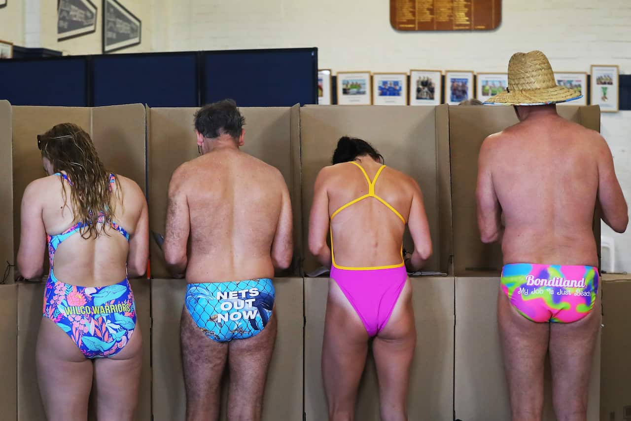 A group of people voting at polling booths, all wearing swimwear.