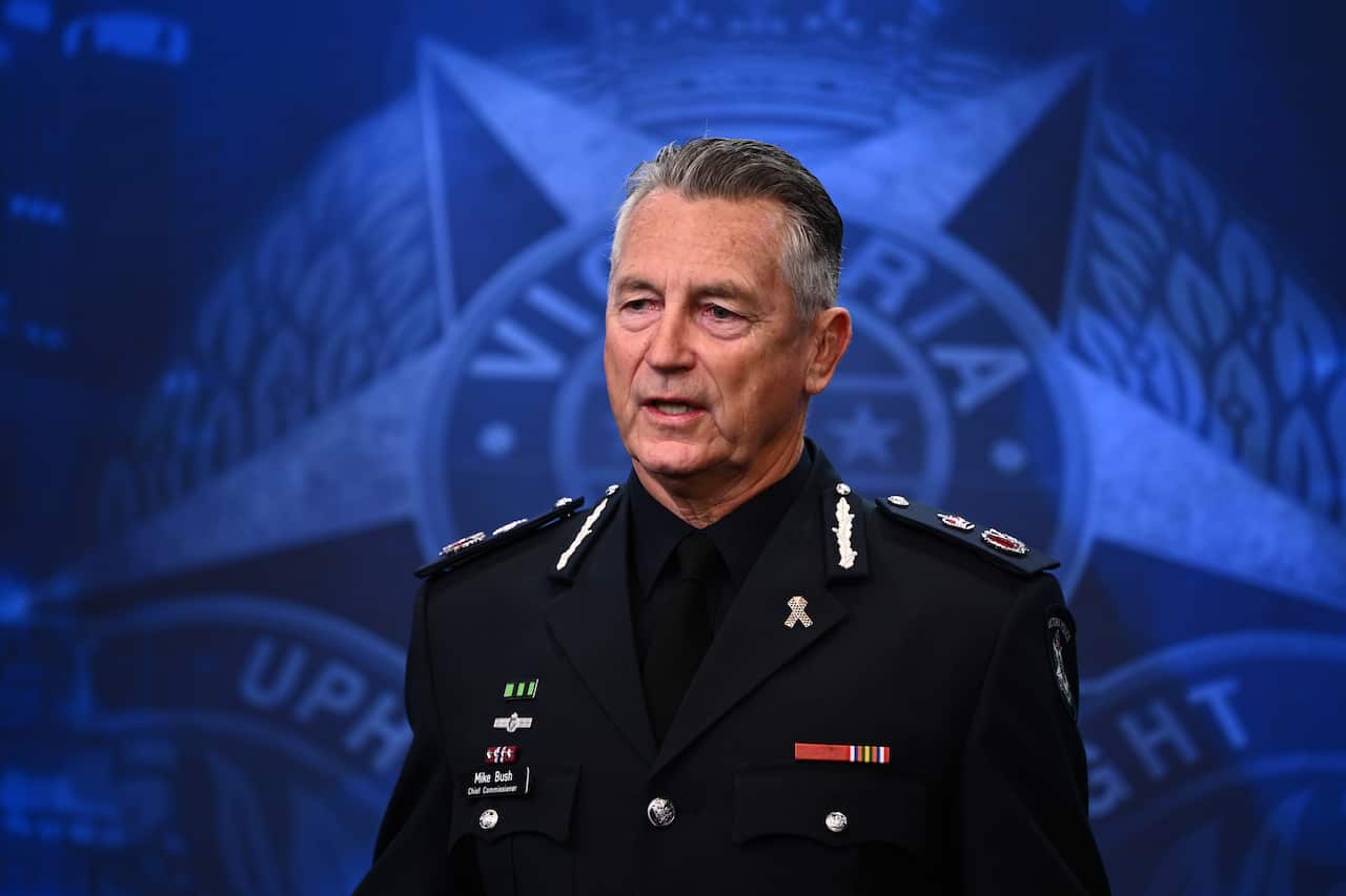 A man in a black police uniform standing in front of a blue wall with a police mural.