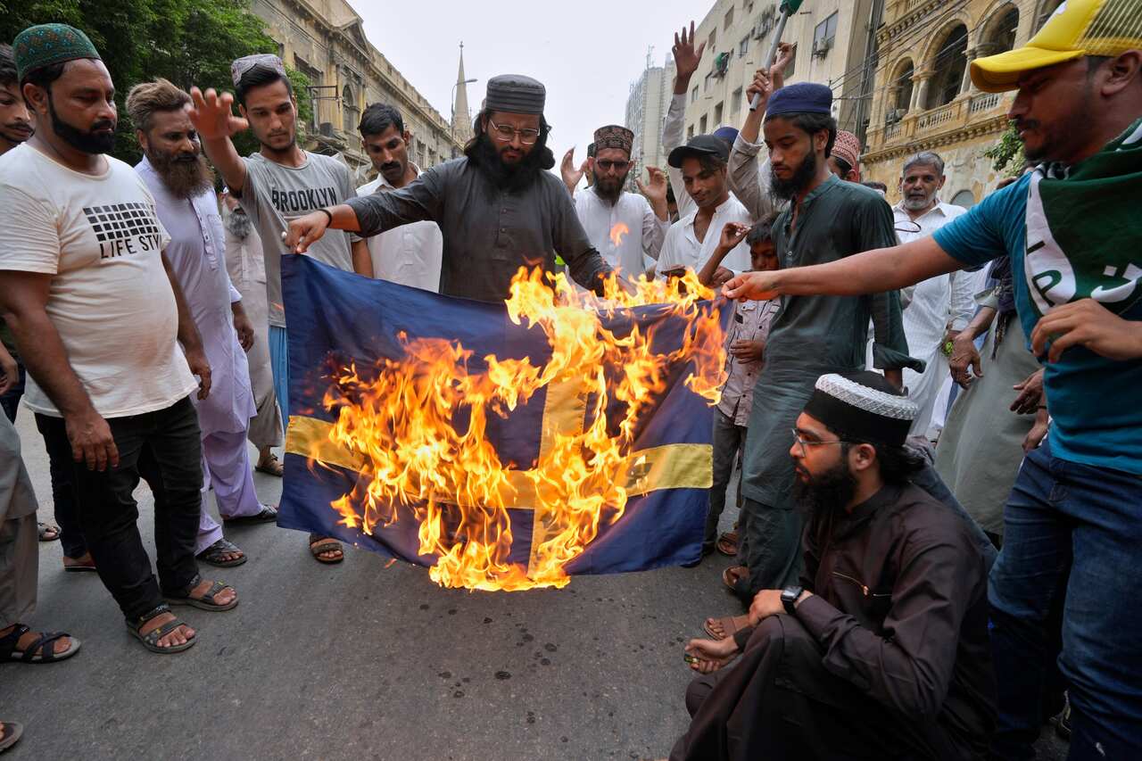 Several men hold a burning Swedish flag as others watch on 