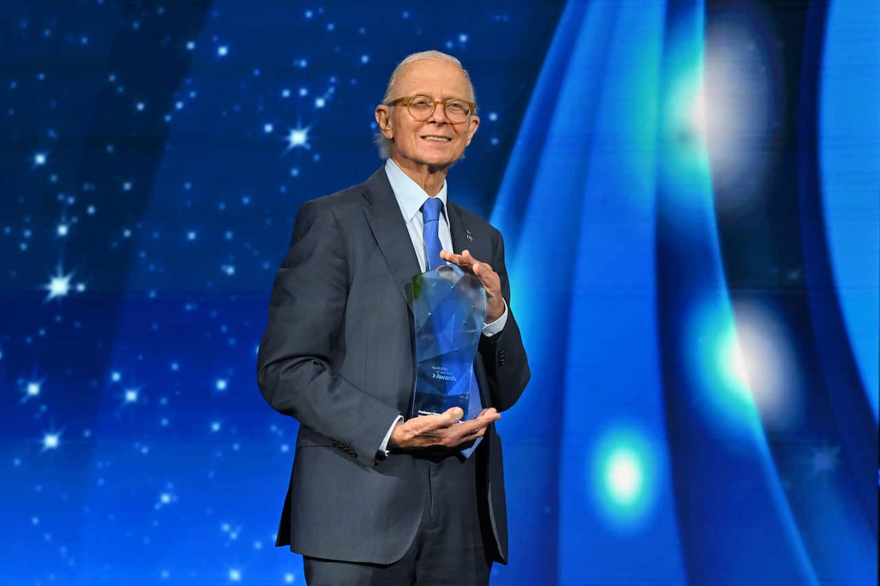 A man in a grey suit holding an award in front of a blue background