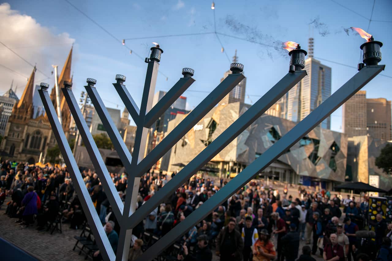 A menorah stands with 3 candles burning during a Chanukah - Pillars of Light public event