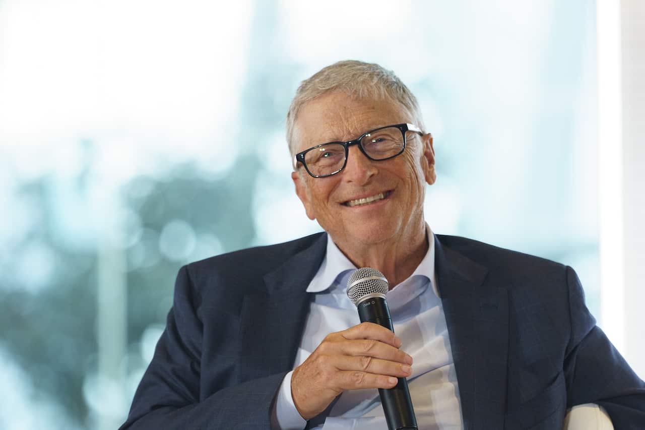 Bill Gates sorri e segura um microfone.