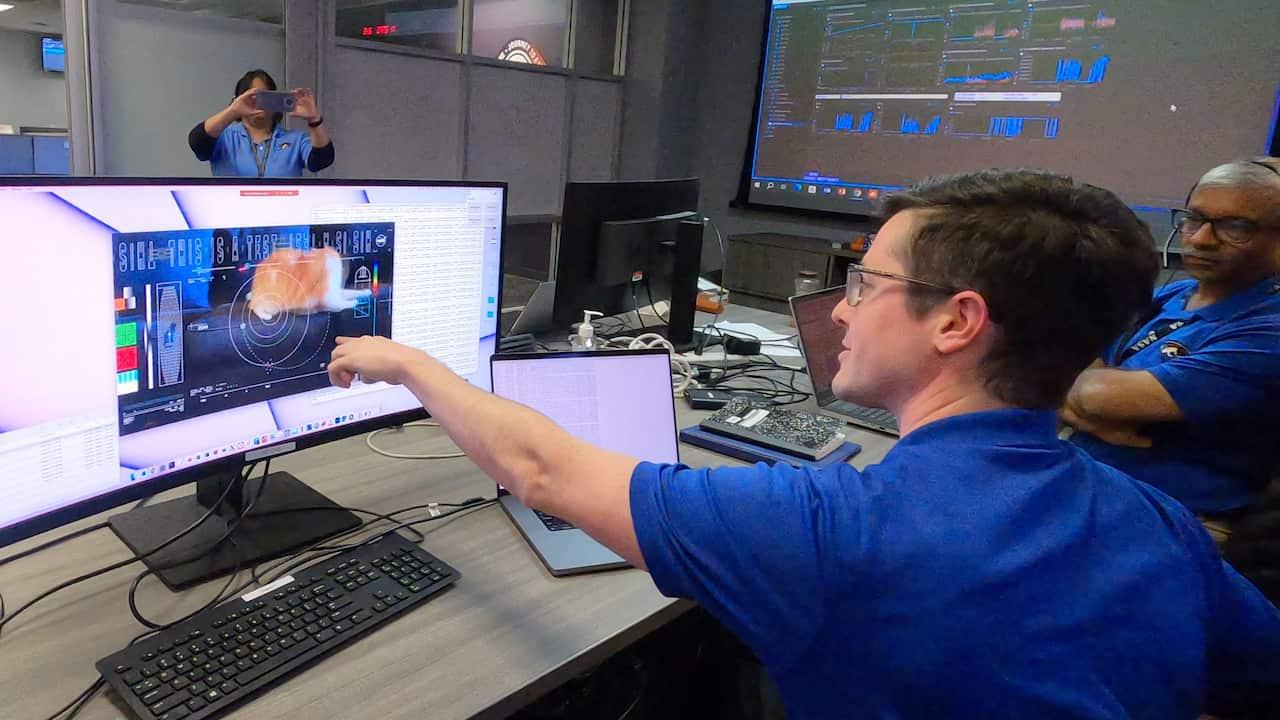 A man wearing a blue shirt points at a computer screen.