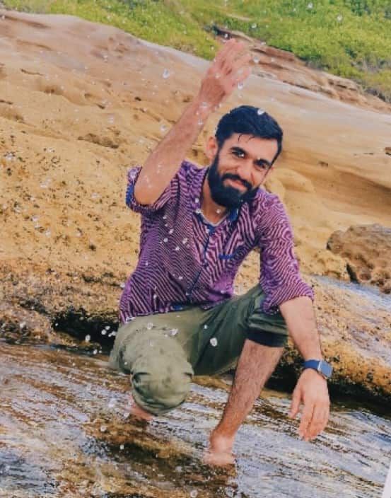 A man kneeling by water, with one hand raised in the air. 