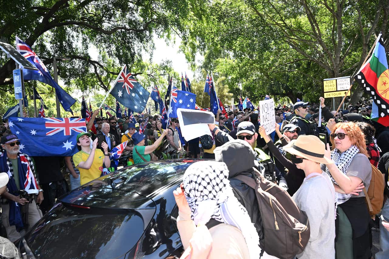 A group of protesters holding up Australian flags is separated by police from a gorup of protesters, many of whom are wearing keffiyeh scarves.
