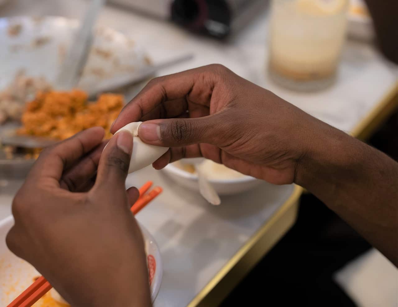 A pair of hands holds up a raw dumpling, sealing the edges tight.