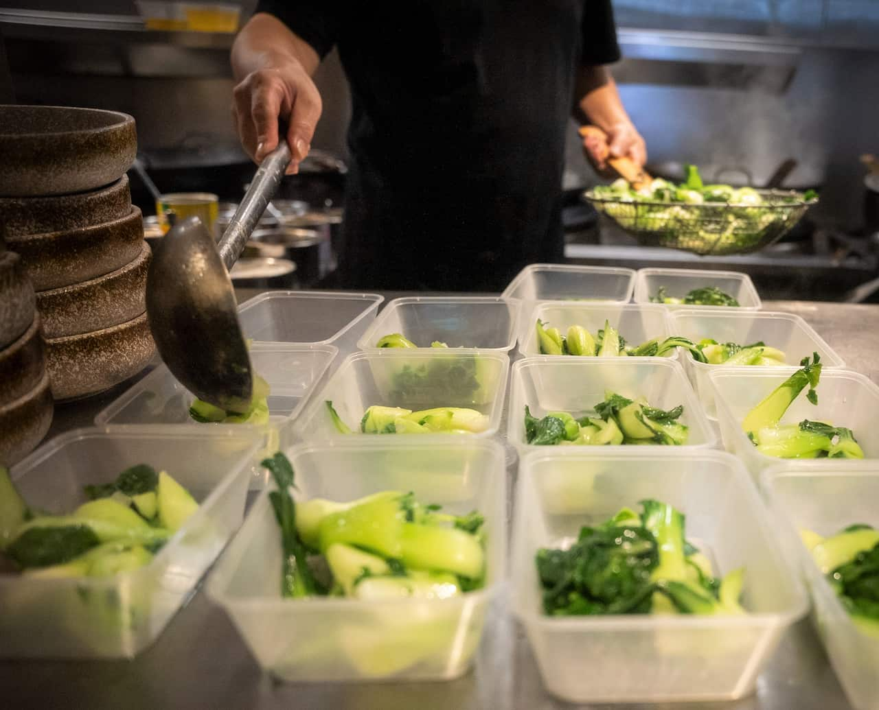 A man ladles green vegetables into plastic containers.