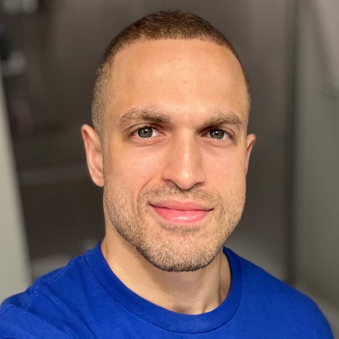 A portrait shot of a man in a blue top with a light smile on his face.