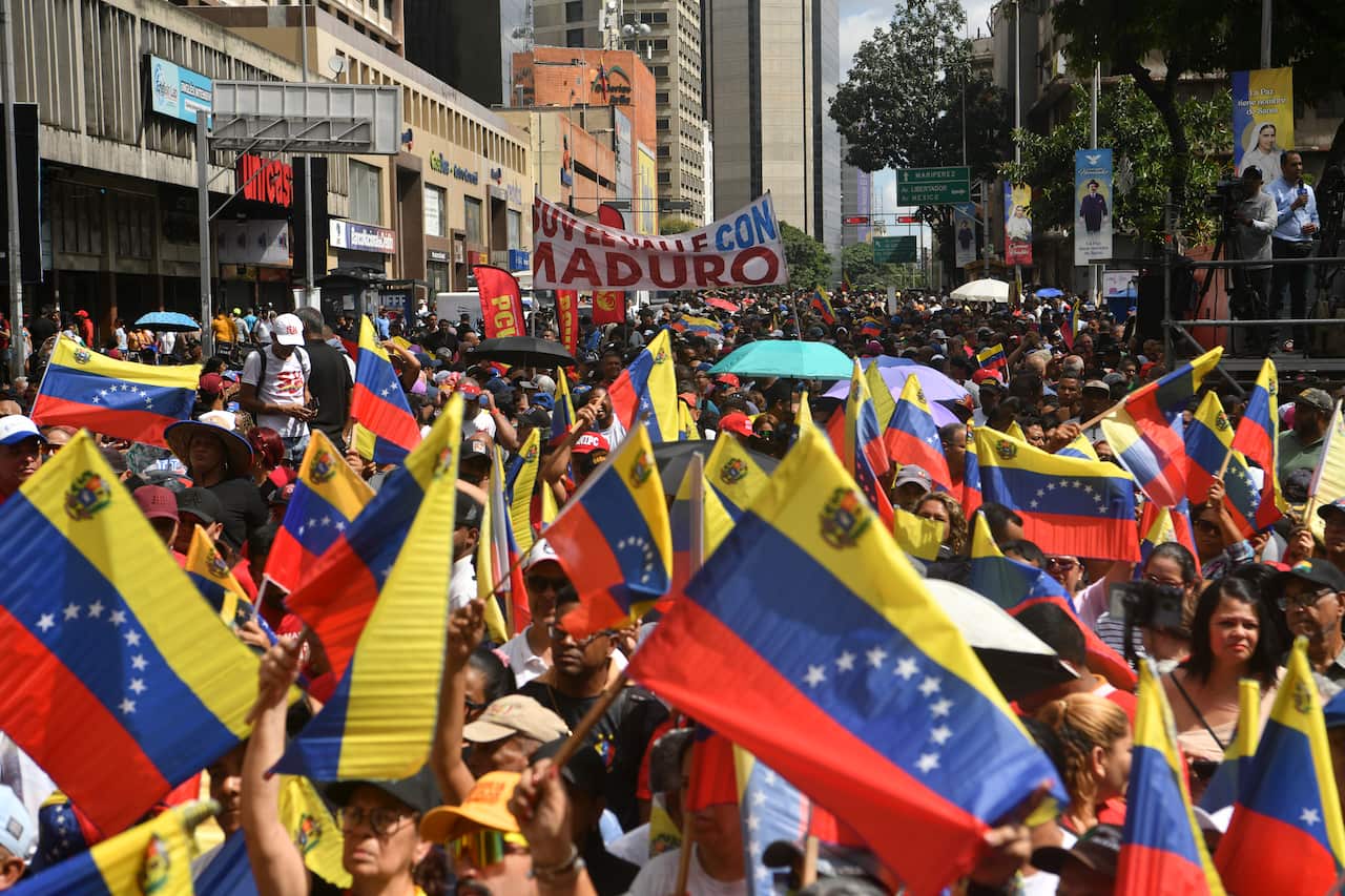 A large crowd of people walking down a street, waving Venezuelan flags.