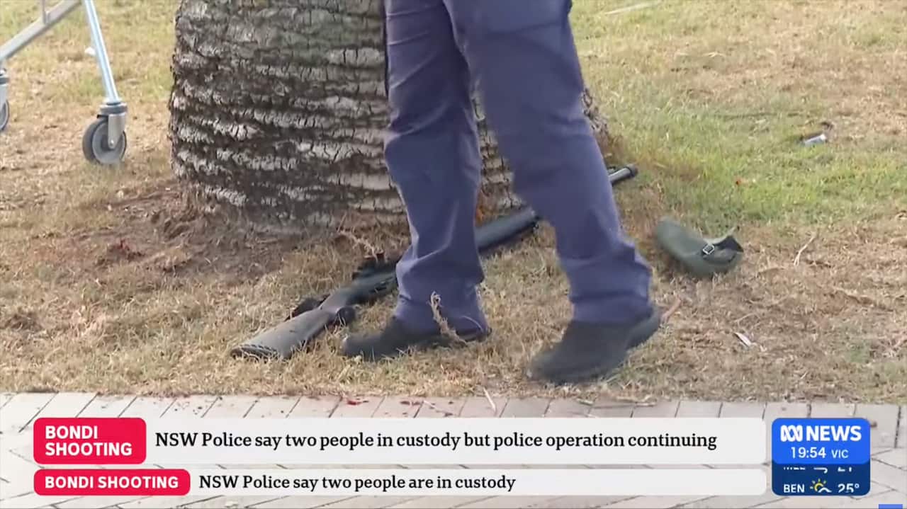 A snapshot from an ABC News broadcast on the Bondi shooting showing a person's legs with weapons on the ground. A ticker is running at the bottom.