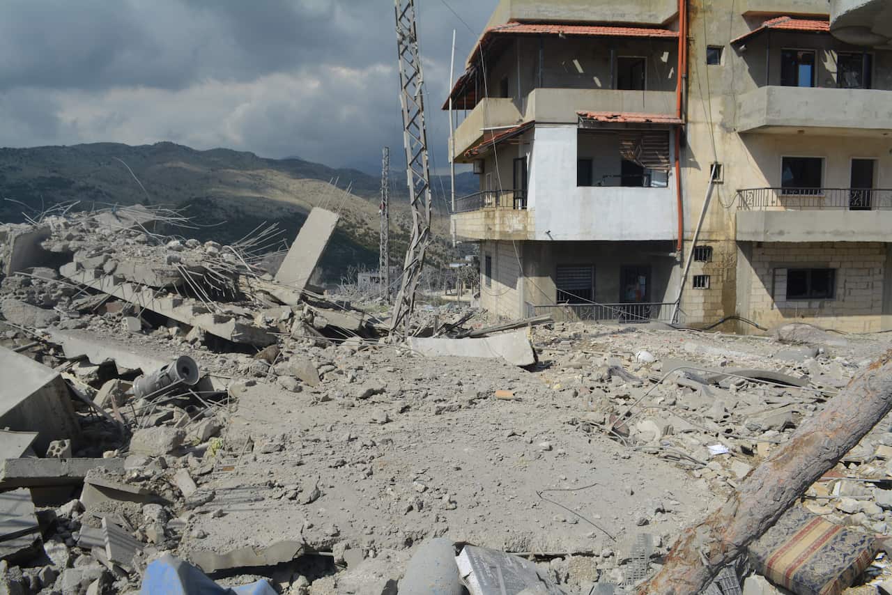 The ruins of a building with a blue sky and a standing building visible 