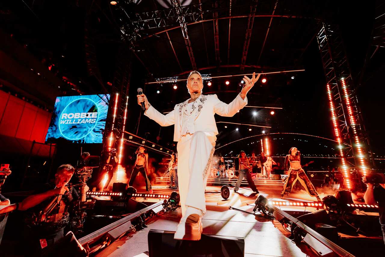 A man performing on a stage wearing a white suit.