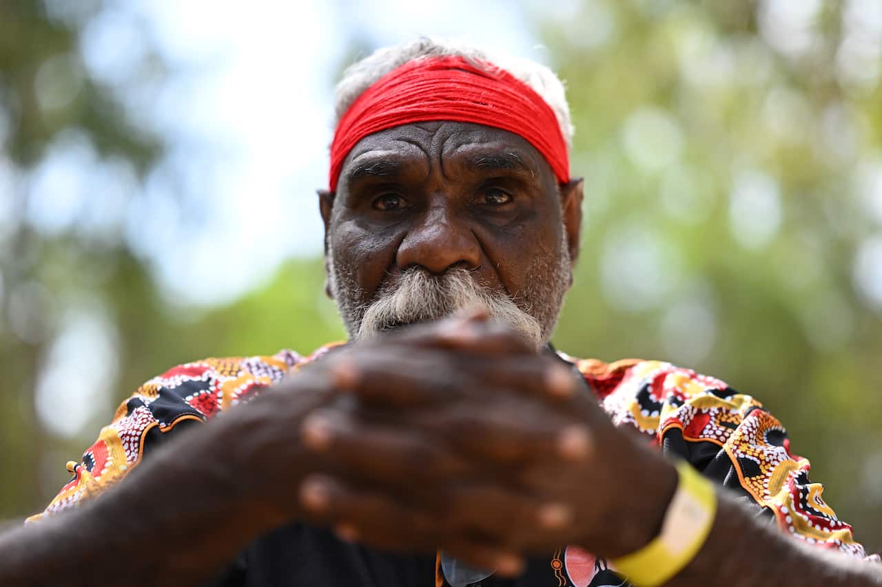 A man's hands clasped together, he wears a black, orange and red shirt and wears a red head band