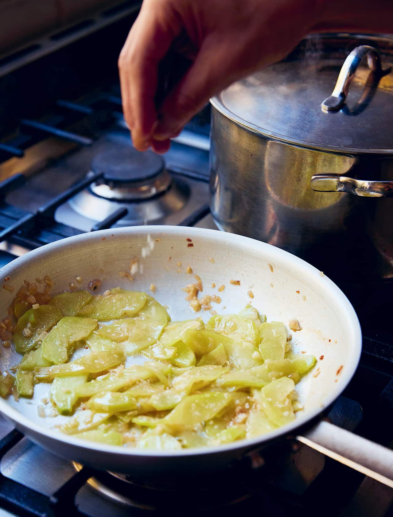 Stir-fried sliced choko in a steel pan on a stove top. 