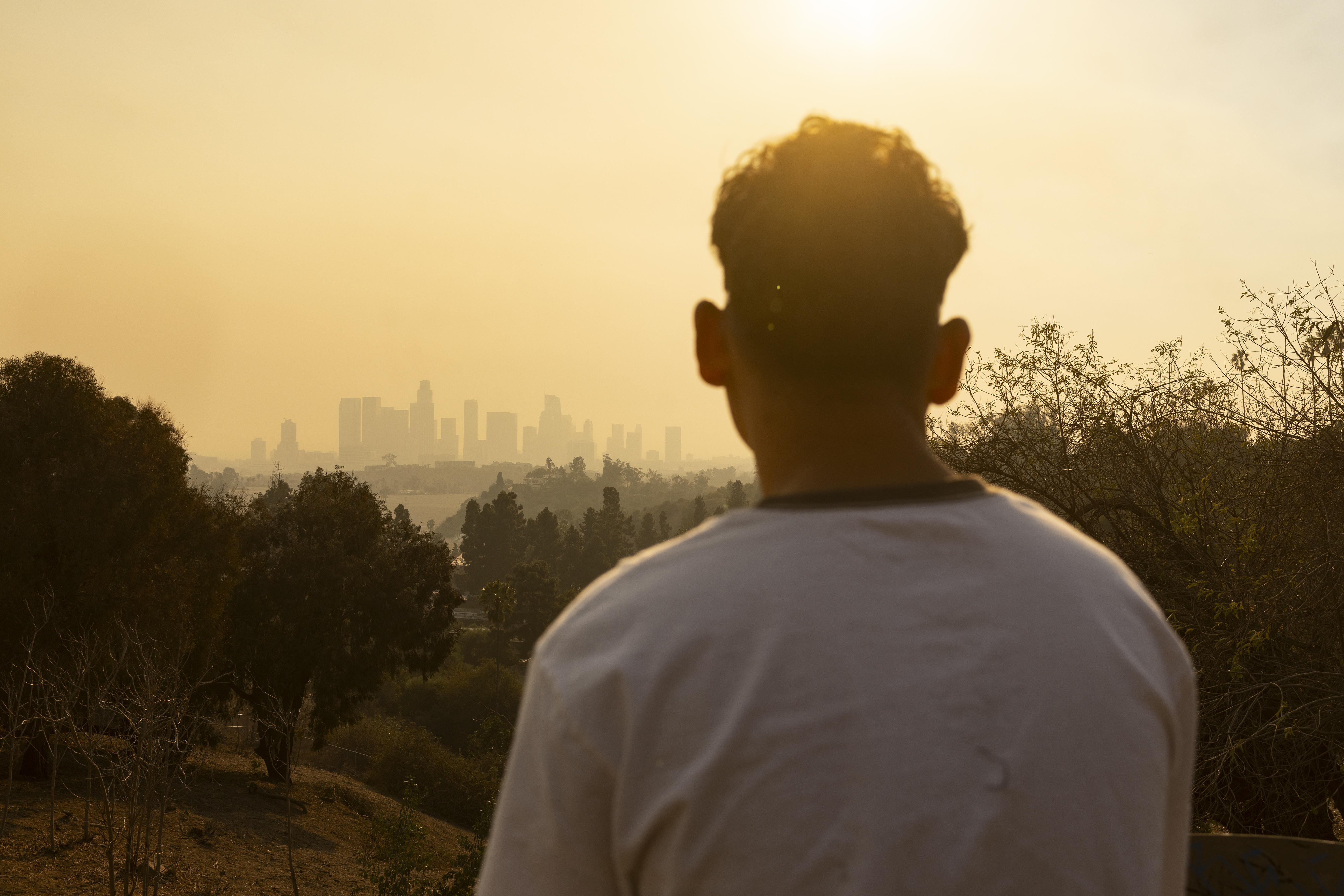 Kebakaran hutan di Los Angeles: Jam malam diberlakukan di beberapa wilayah saat warga bergulat dengan kehancuran 2 Seseorang memandang ke Los Angeles, dengan langit tertutup kabut oranye.