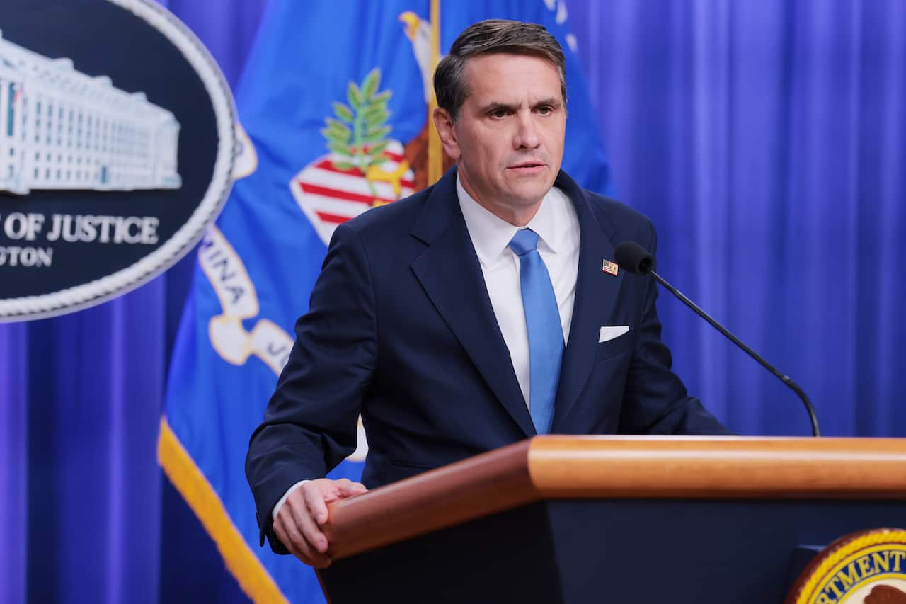 A middle-aged white man wearing a navy suit and tie speaking before a lectern