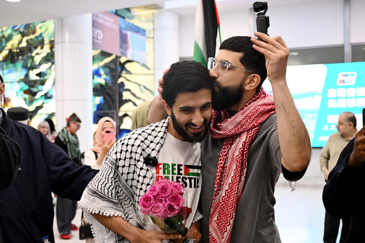 A man holding pink roses is embraced by another man.