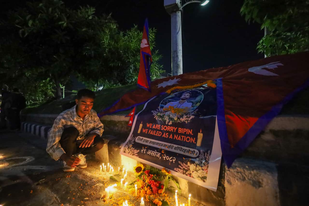 A person is lighting candles next to a poster of a young man at night.