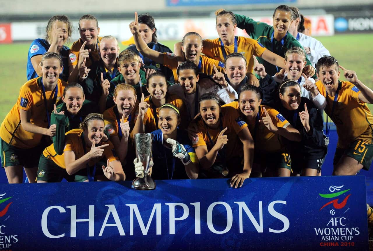 Women in yellow football jerseys celebrating in front of a banner that says CHAMPIONS