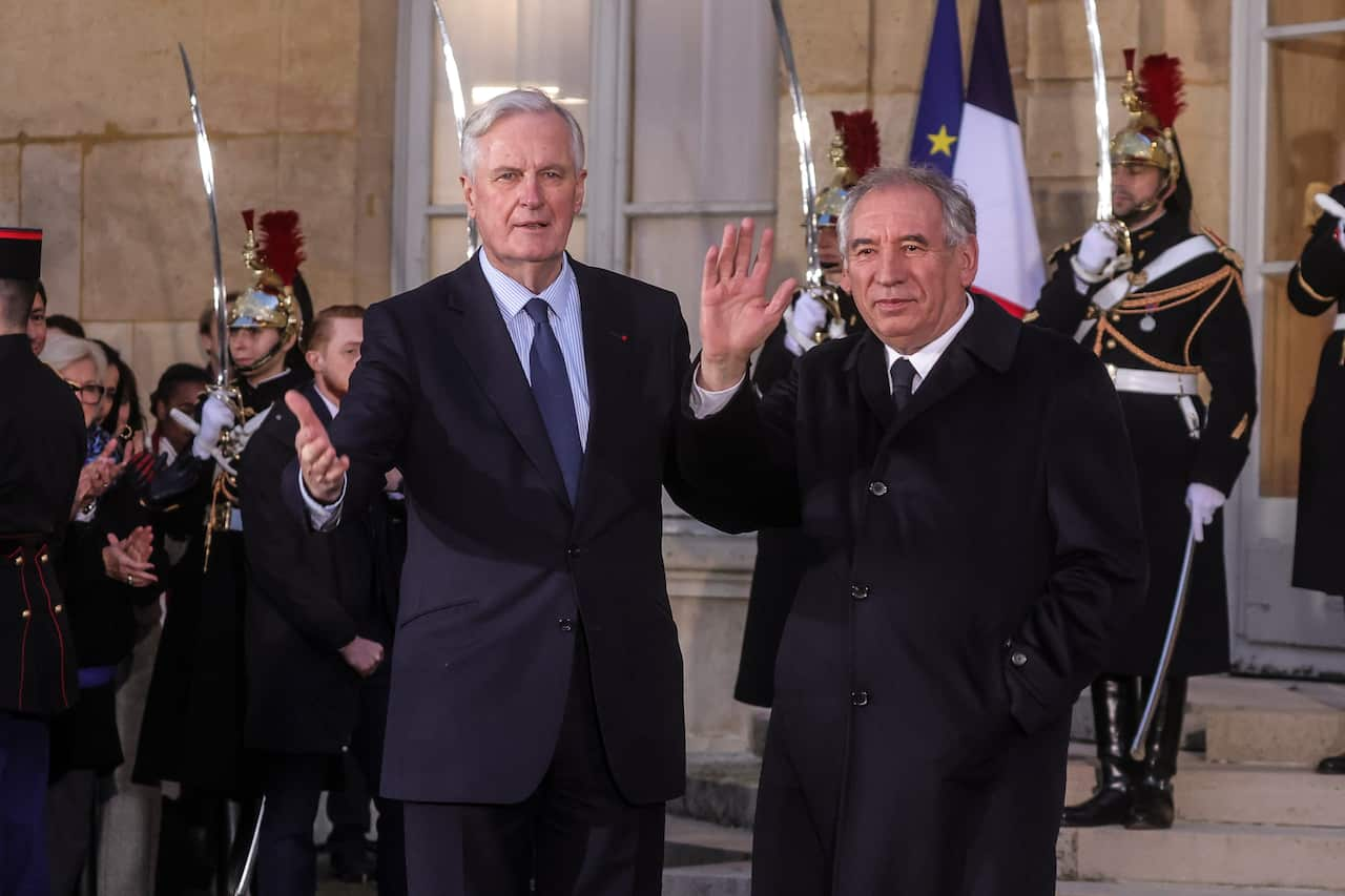 Two men in suits standing and waving next to each other.