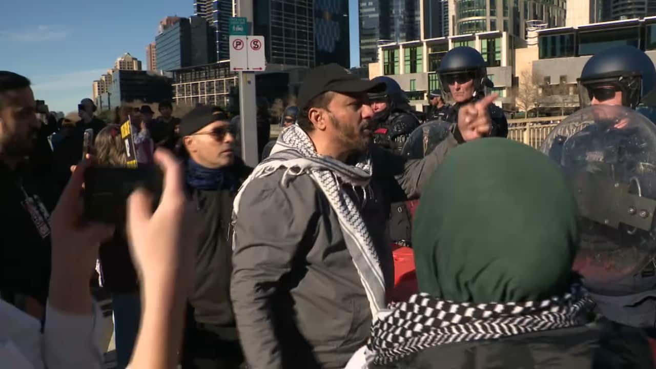 A man with a Palestinian keffiyeh wrapped around his neck argues with riot police