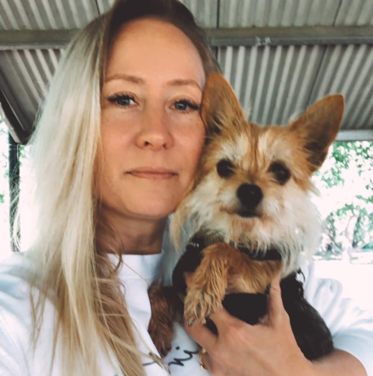 A blonde woman holding a small dog in her hand.