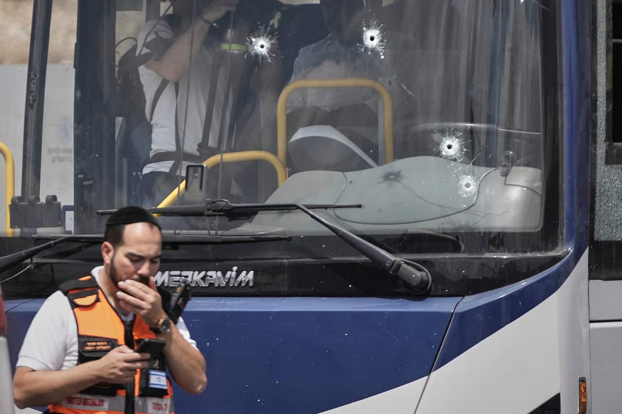 A bus front window with bullet holes in it. A man in front is holding his mouth.