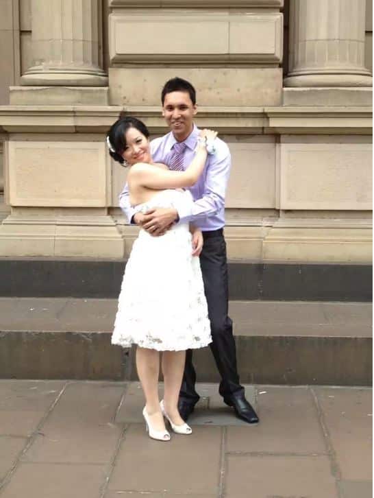 A woman and man embrace each other in front of stone columns.