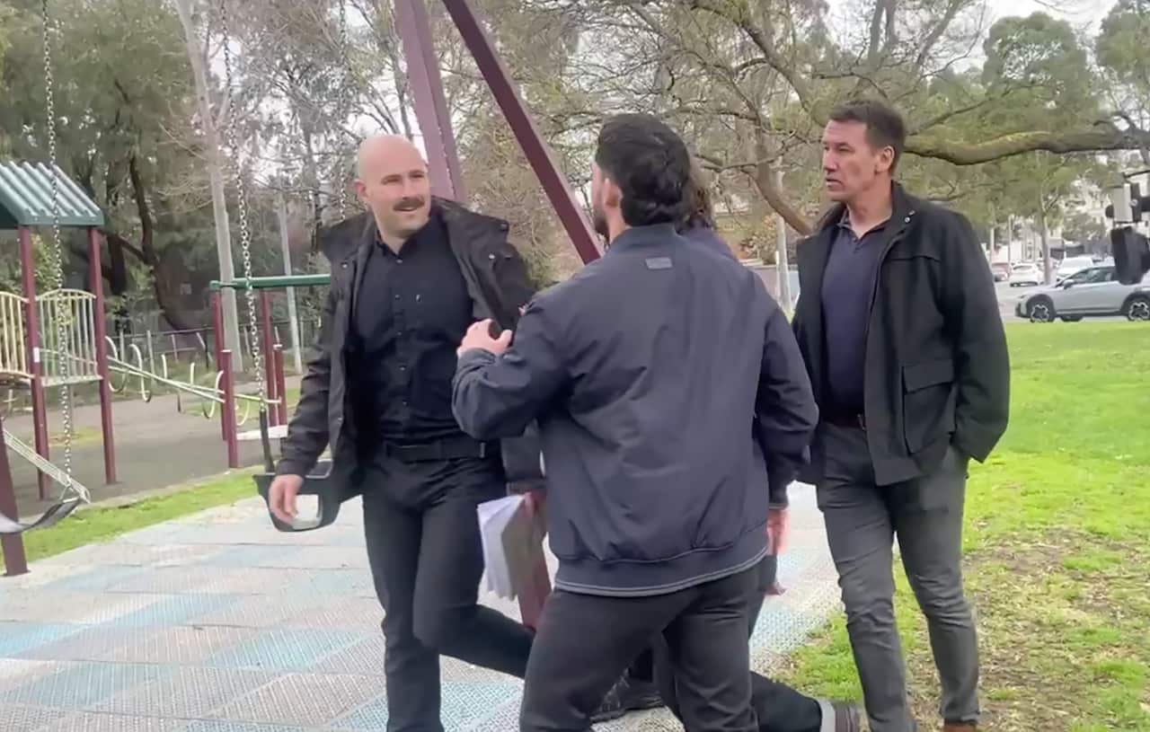 A man in an all black outfit smiles with three men standing close to him next to a playground. 