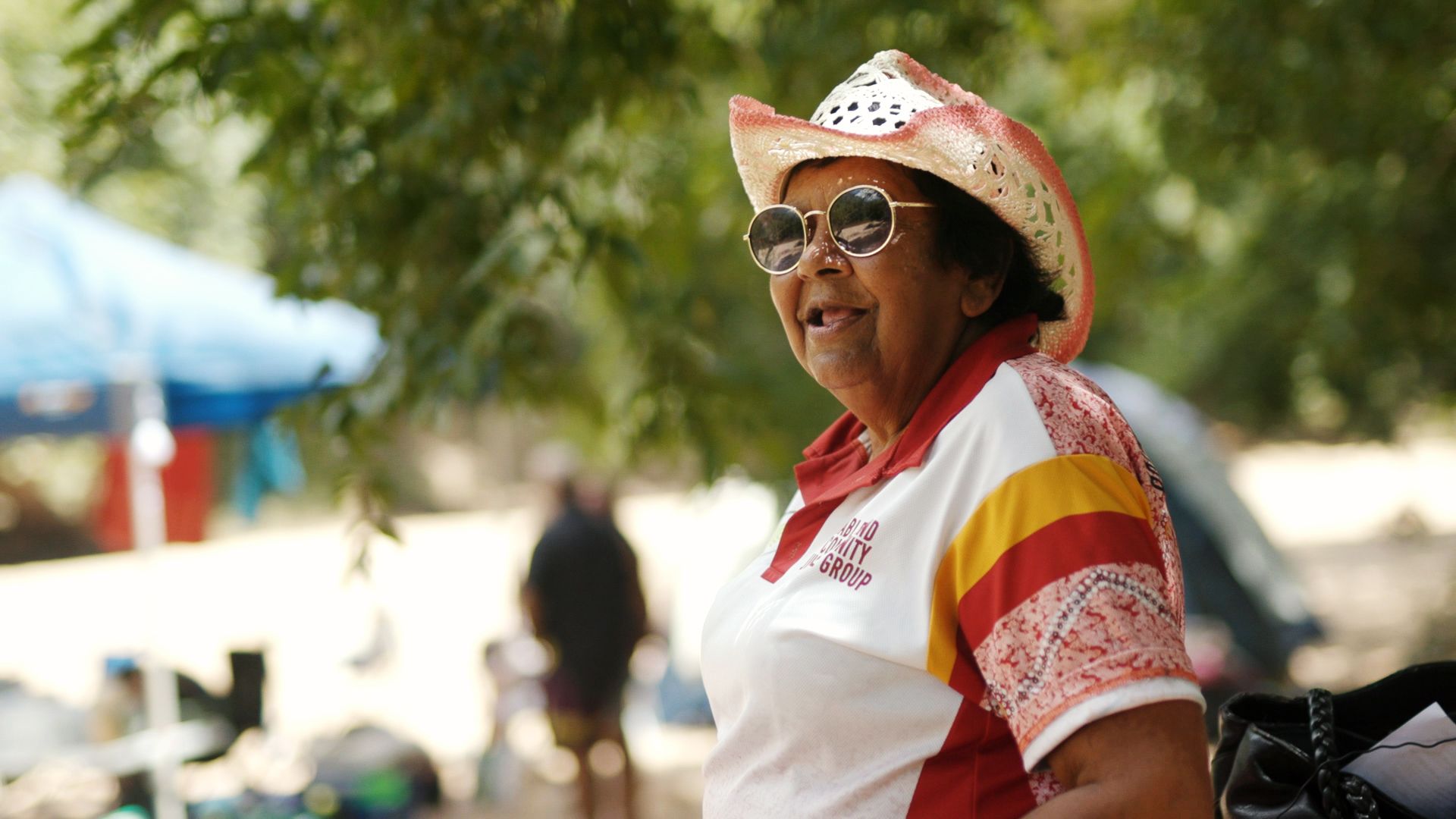 Image of Rhonda Doolley in a hat, standing in front of trees near a creek bed.