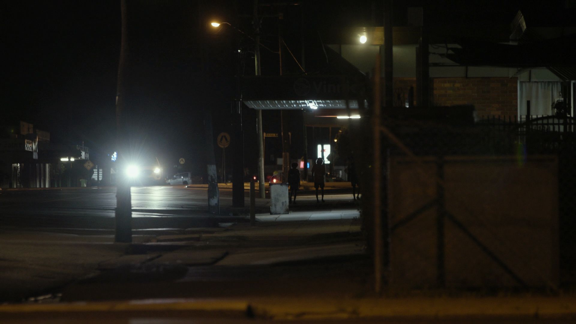 A North Queensland street at night, with car headlights and people in the distance 