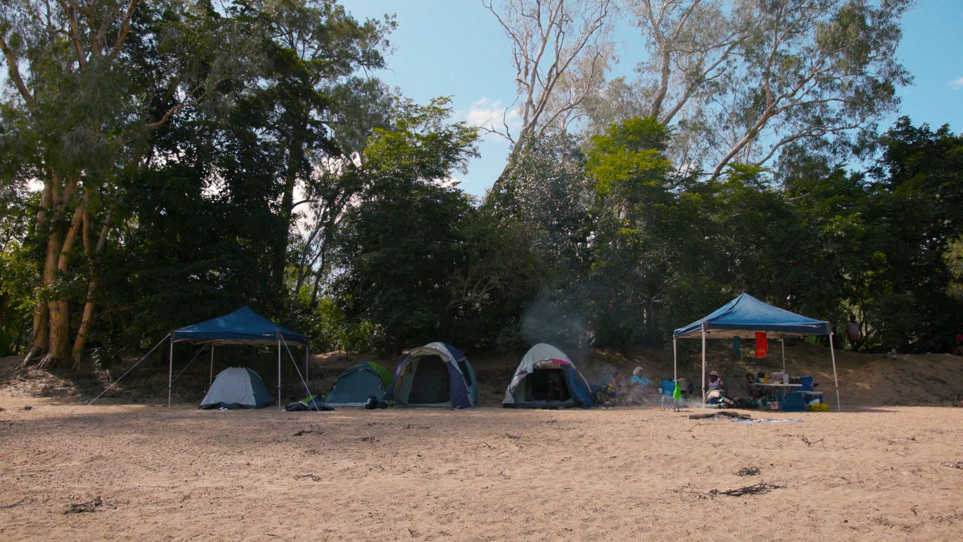Image of tents on a beach in North Queensland, with people sitting and cooking.