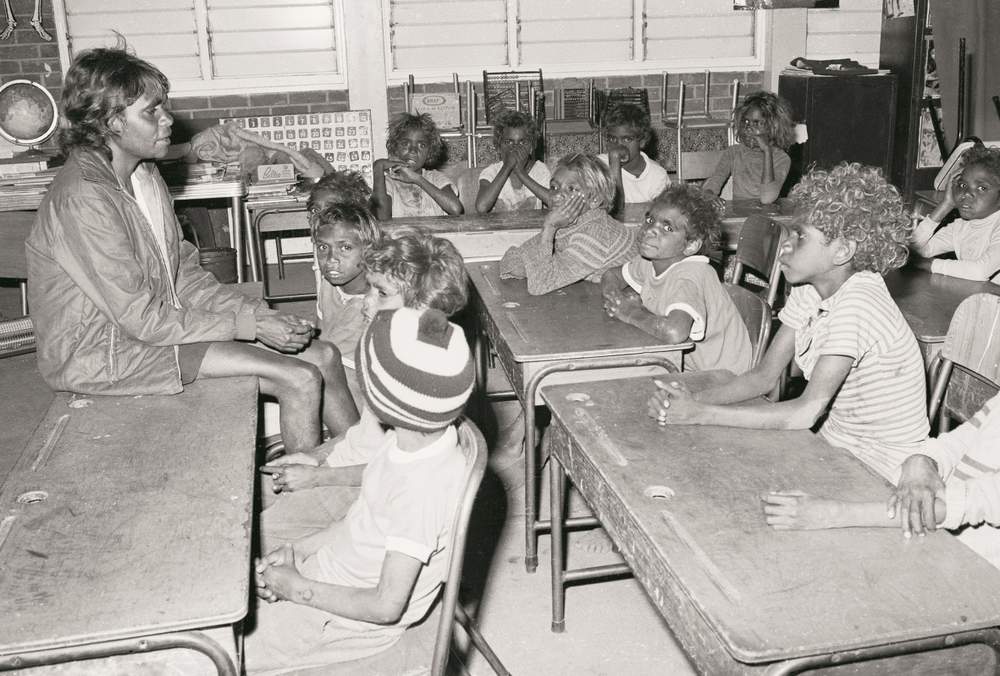 Tess Ross teaching a class Yuendumu School, 1964, with Francis Kelly (wearing the beanie) in the front row. (Image: Nation Archives Australia: A8739\/1, 11645325)