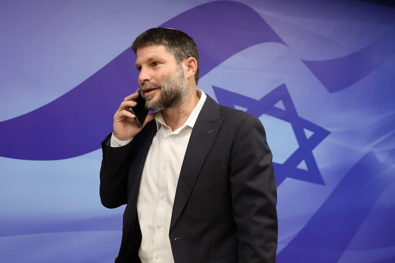 A man in a dark suit and white shirt holding a phone to his ear.