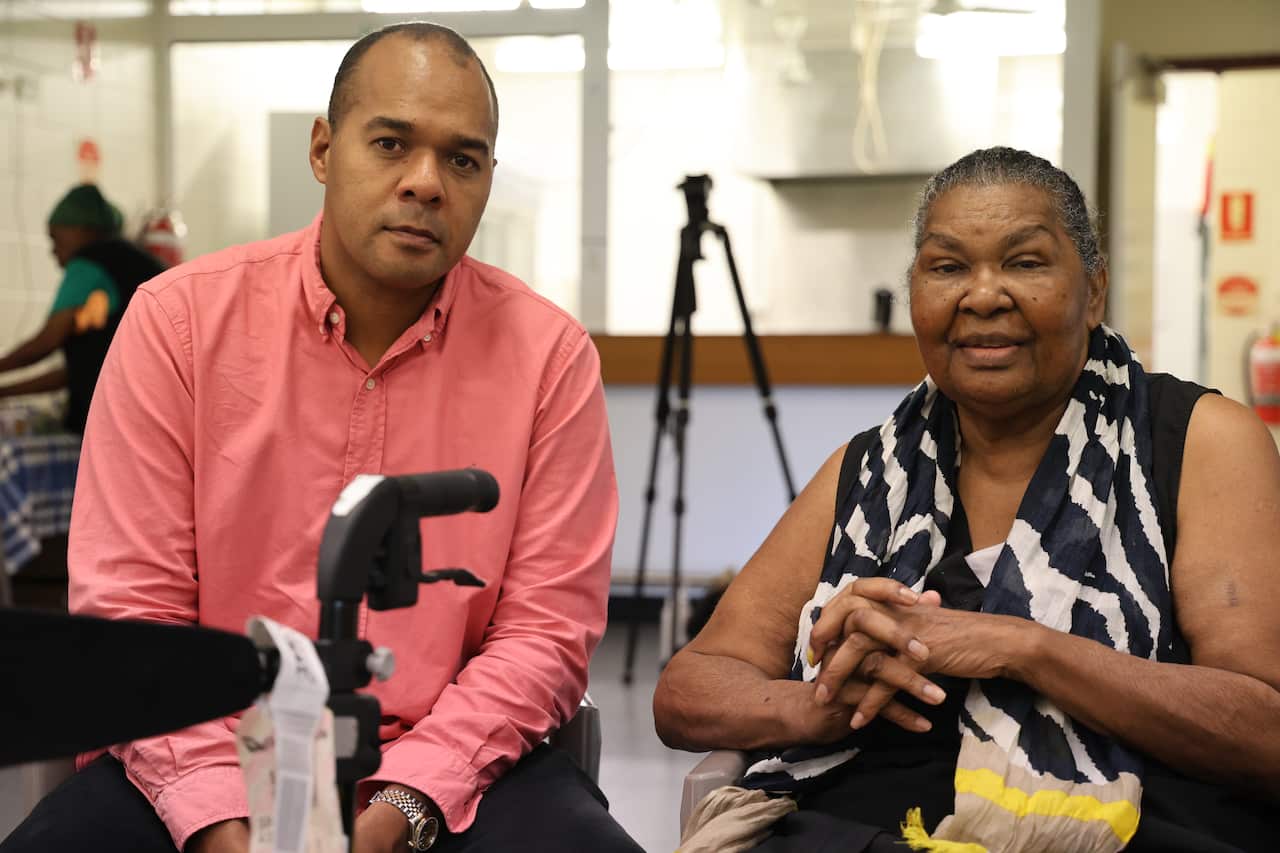 Prominent Indigenous Barrister Joshua Creamer sits next to a Thursday Island resident in a hall.